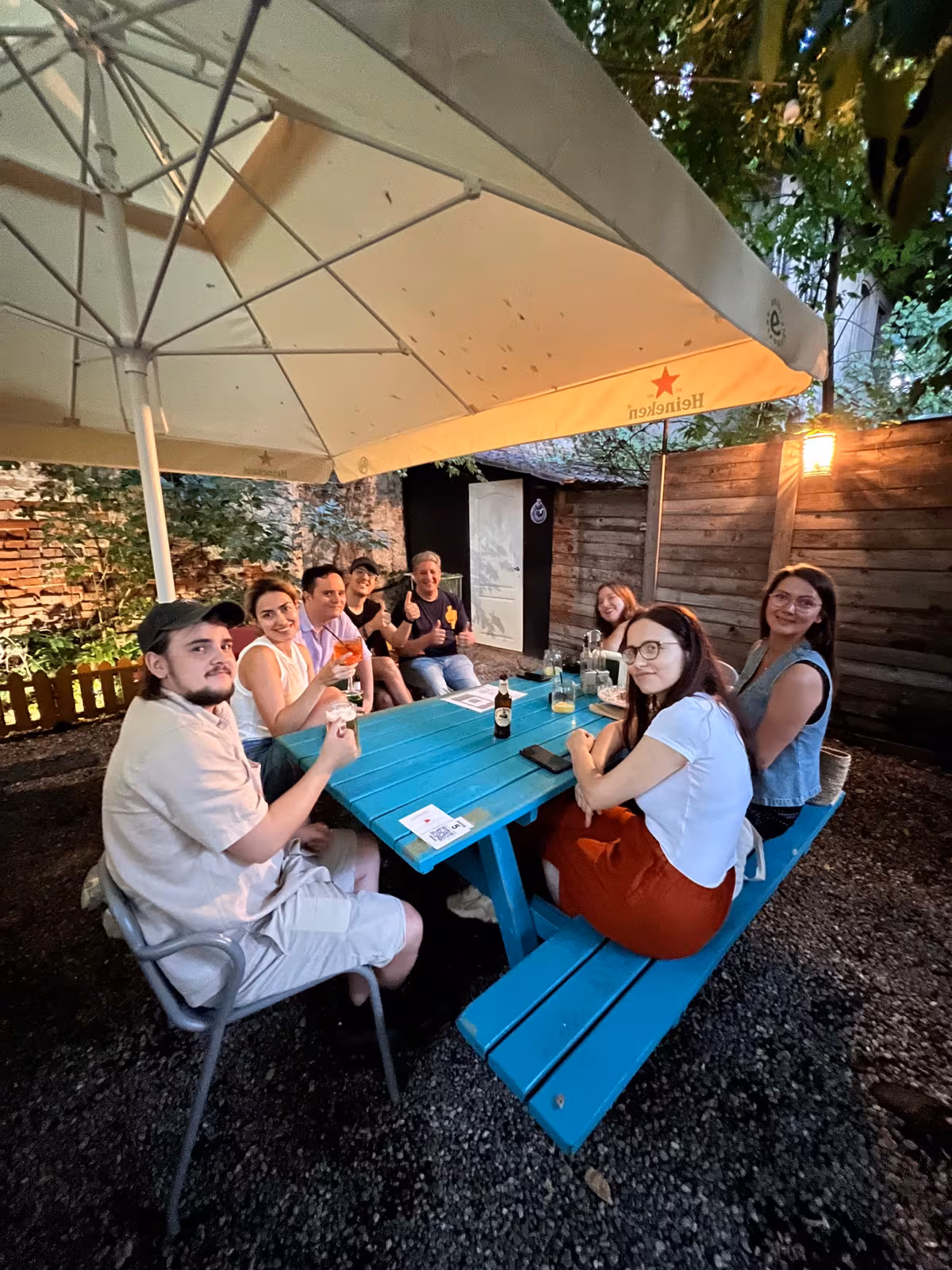 A small group at a blue picnic table under a parasol