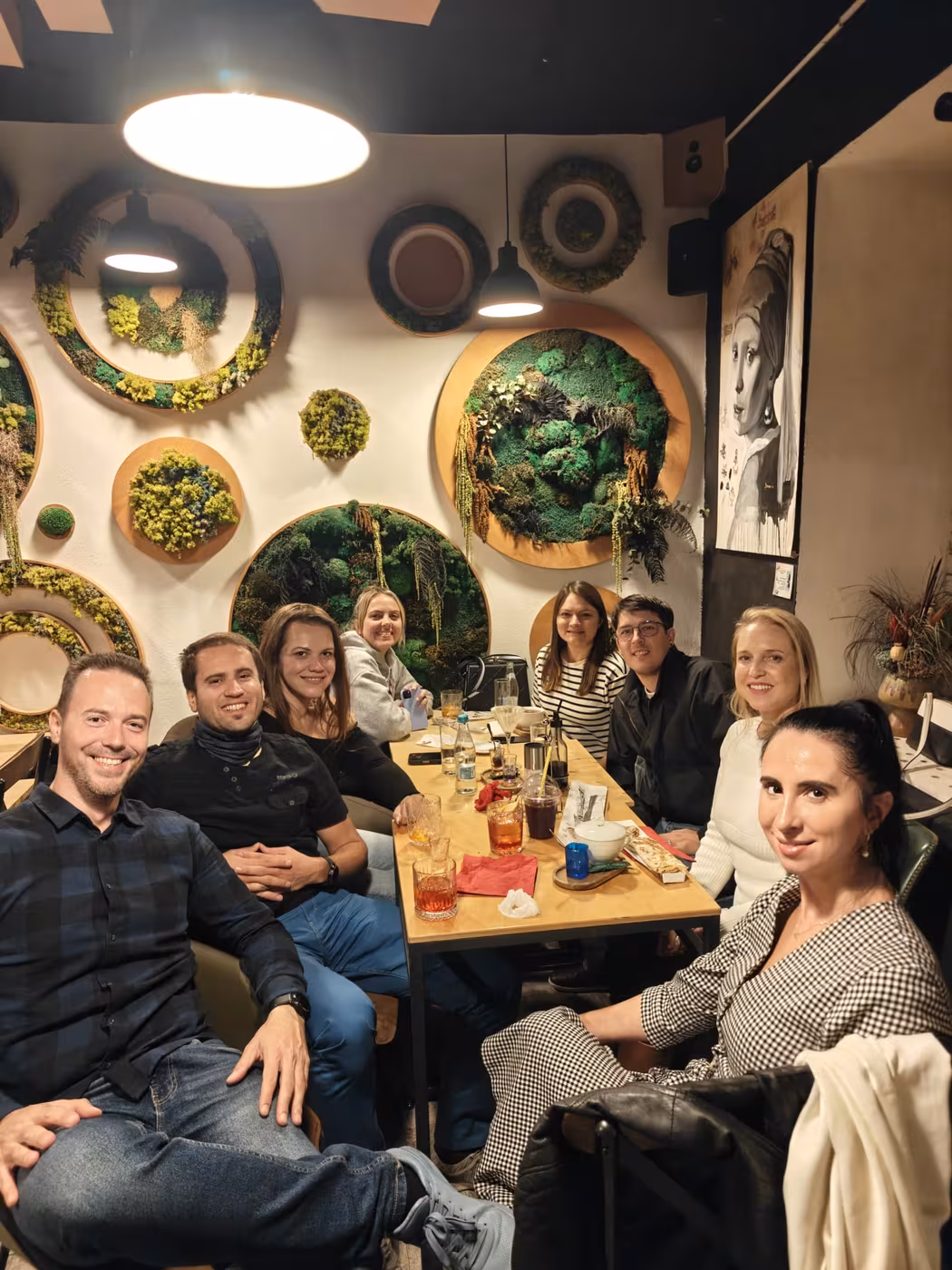 Eight members at a group dinner in front of a wall of moss art
