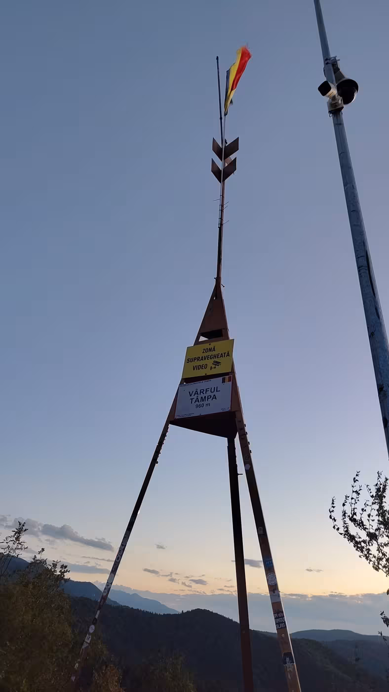 The Tâmpa summit marker at 960 m with a Romanian flag, at dusk