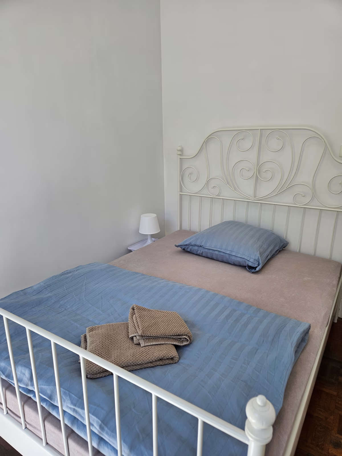 A double bed with a white wrought-iron frame, blue bedding and folded towels