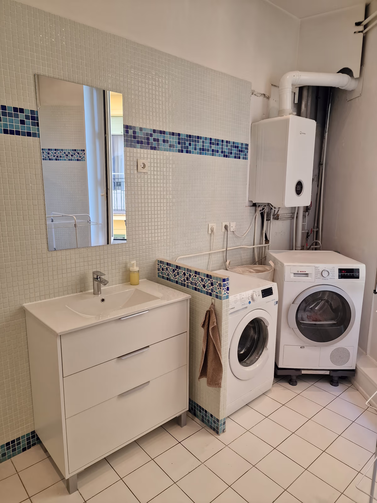 The laundry corner of the second bathroom, with a washbasin, a washing machine and a dryer