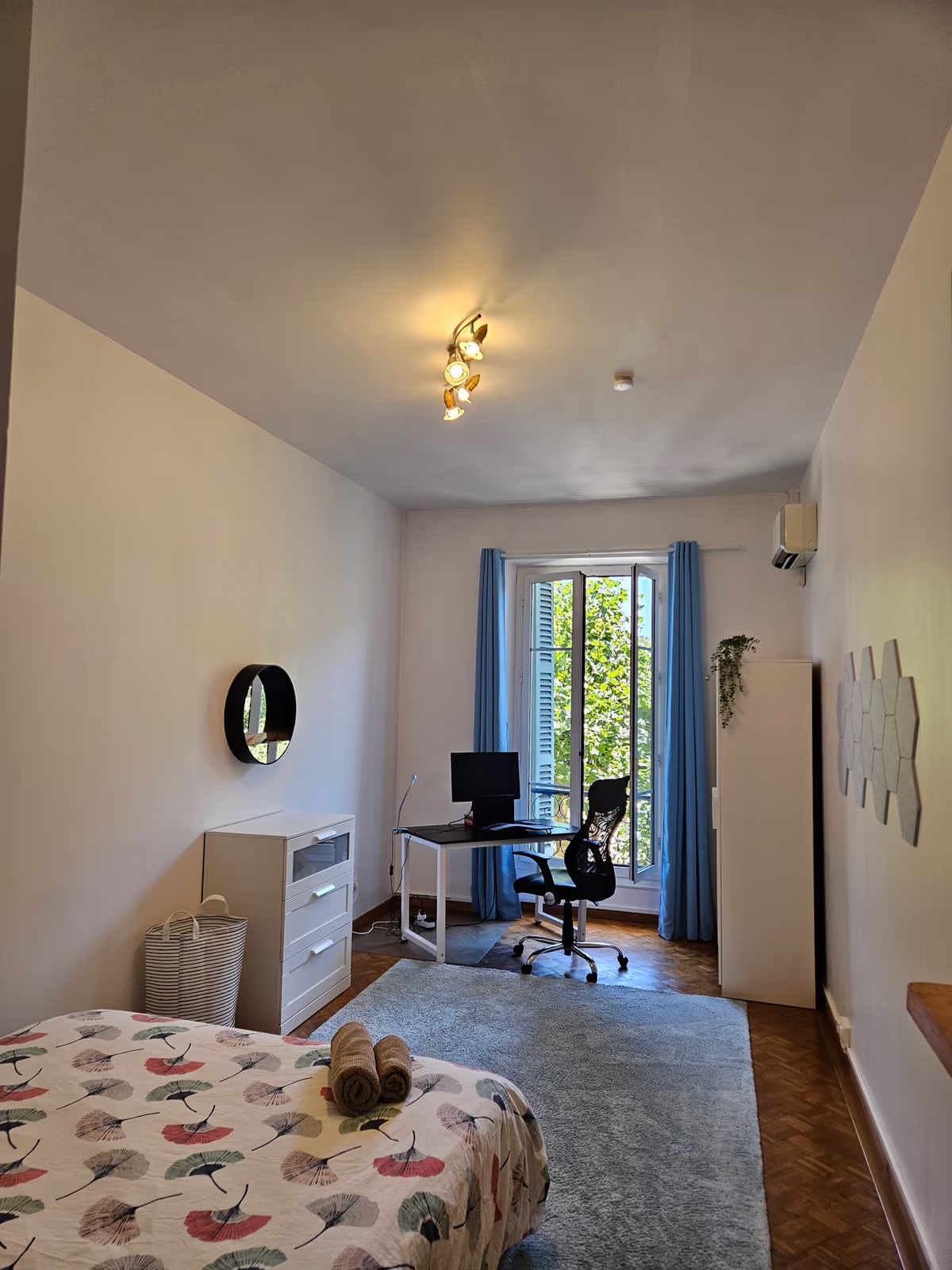 The queen room, with a patterned bedspread, a chest of drawers and a desk by the balcony door