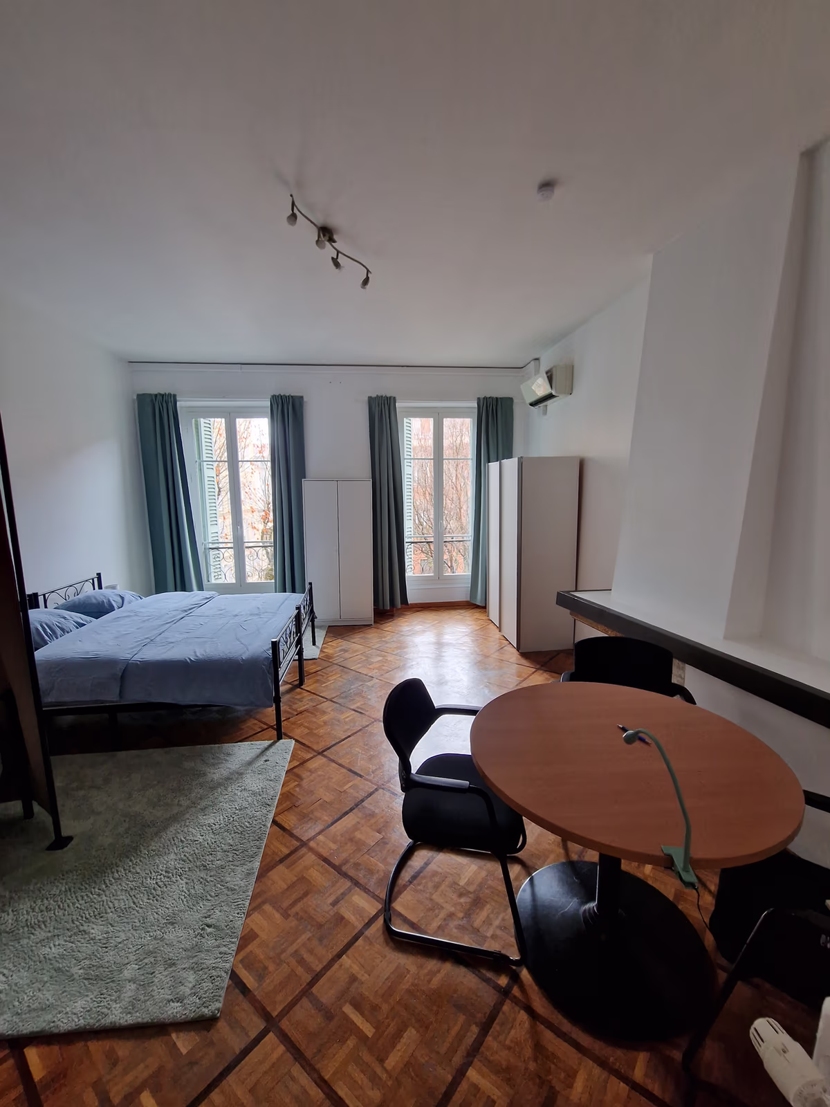 The twin XL room, with two tall windows, a bed and a round table on parquet floors